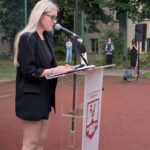Uczennica przemawia zza mównicy z logo szkoły podczas inauguracji roku szkolnego.